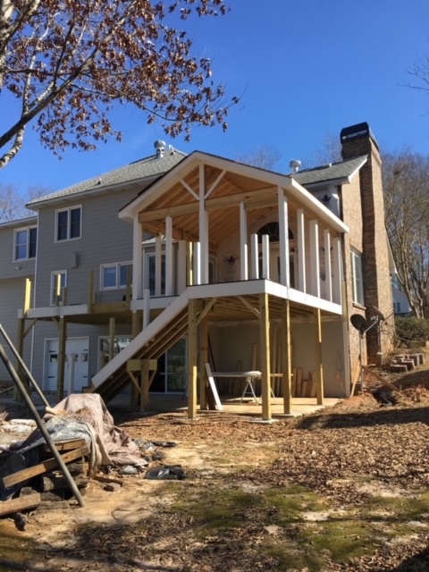 back of large home with wooden deck and screened porch being constructed.